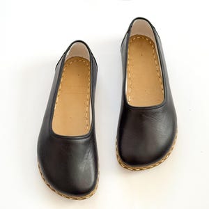 May include: A pair of black leather flats with a rounded toe and a tan insole. The shoes have a stitched sole and a simple, classic design. The shoes are likely for everyday wear.