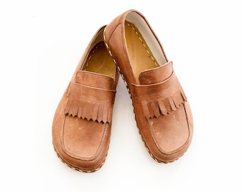 May include: A pair of brown leather loafers with a fringed vamp. The shoes have a classic design with a rounded toe and a slip-on style. The soles are stitched with a contrasting thread.
