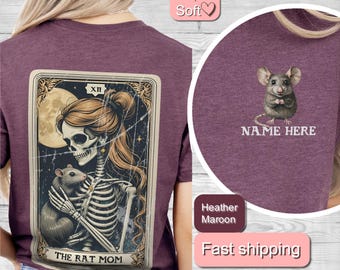 May include: A maroon t-shirt with a graphic of a skeleton holding a rat. The graphic is in the style of a tarot card and says "The Rat Mom" at the bottom. The t-shirt also has a small graphic of a rat on the upper right side with the text "Name Here".