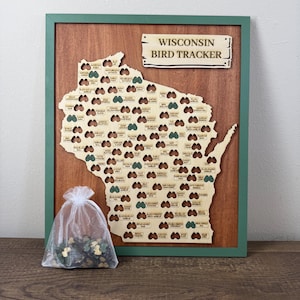 May include: A framed Wisconsin Bird Tracker wooden map featuring laser-cut slots for bird-shaped tokens. The map includes a sign labeled "WISCONSIN BIRD TRACKER" and a sheer white drawstring bag filled with small, green, bird-shaped wooden tokens.