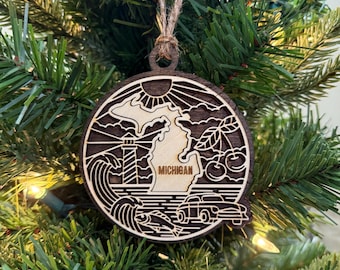 May include: Wooden Christmas ornament featuring a detailed laser-cut design of the state of Michigan. The ornament includes a lighthouse, waves, cherries, and a vintage car. The word "MICHIGAN" is also visible.