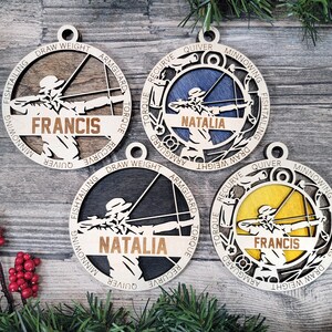 May include: Four wooden archery-themed ornaments. Each ornament features a cutout design of an archer with a bow and arrow, the name of the archer, and archery-related words. The backgrounds are in various colors: brown, blue, black, and yellow.