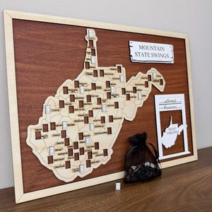 May include: A wooden wall map of West Virginia featuring cutouts for swing locations, labeled with specific site names. The map includes a sign reading MOUNTAIN STATE SWINGS and a separate frame with the text almost heaven WEST VIRGINIA.