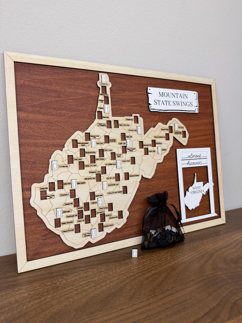 May include: A wooden wall map of West Virginia featuring cutouts for swing locations, labeled with specific site names. The map includes a sign reading MOUNTAIN STATE SWINGS and a separate frame with the text almost heaven WEST VIRGINIA.