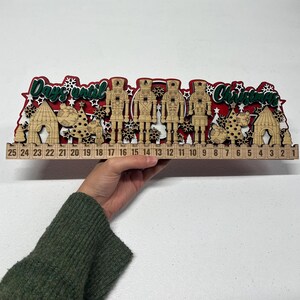 May include: A wooden Christmas advent calendar with the text "Days until Christmas". The calendar features laser-cut designs of nutcrackers, Christmas trees, and houses. Numbers 1-25 are displayed along the bottom.