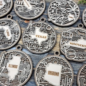 May include: Wooden ornaments featuring state outlines and landmarks. Each ornament is laser-cut with intricate designs and the state name. States include Texas, Kentucky, Arizona, Illinois, Florida, California, Hawaii, and South Carolina.