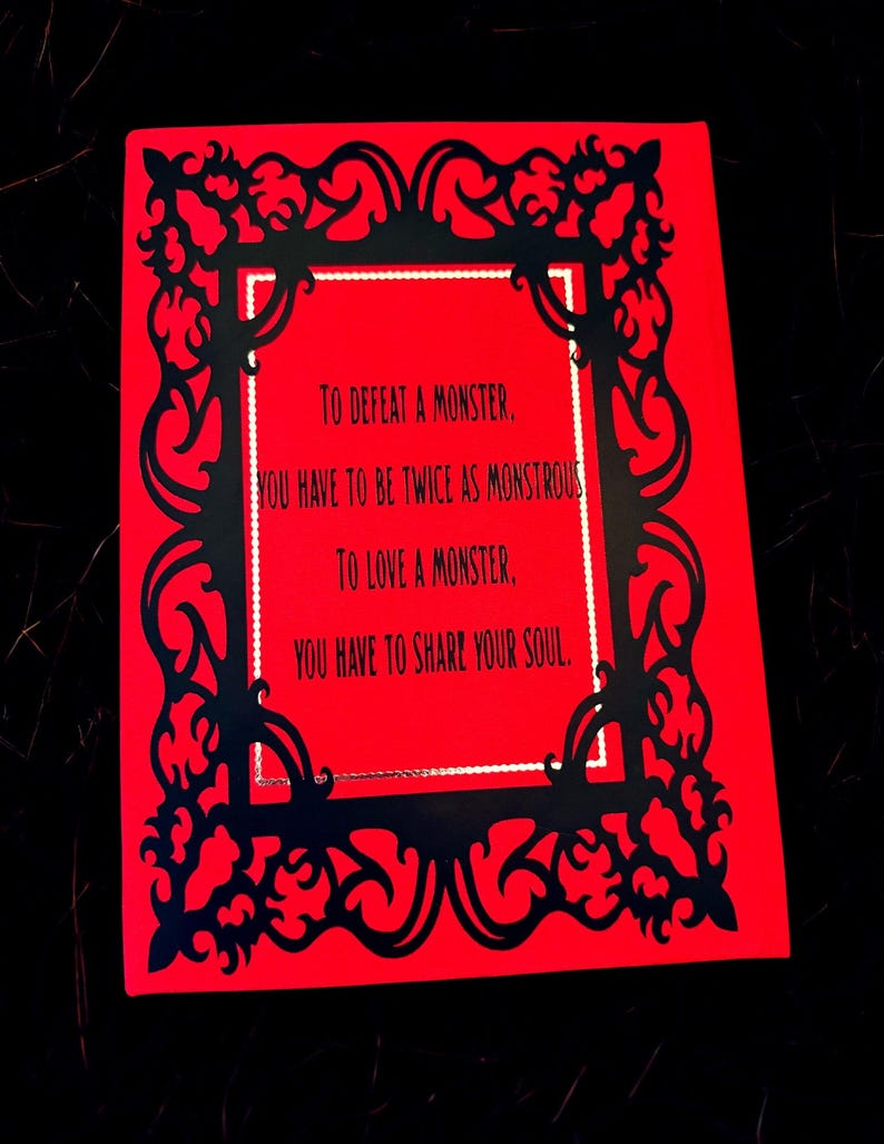 May include: A red card with black filigree border and text that reads: "TO DEFEAT A MONSTER, YOU HAVE TO BE TWICE AS MONSTROUS, TO LOVE A MONSTER, YOU HAVE TO SHARE YOUR SOUL."