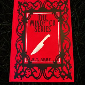May include: A red book with the title "THE MINDF*CK SERIES" and a silver knife illustration. The book cover has a black decorative frame and the author's name, S.T. ABBY, is printed at the bottom. The book is set against a dark green background.