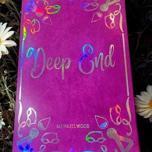 May include: A purple book with a holographic cover featuring the title "Deep End" and the author's name "Ali Hazelwood".