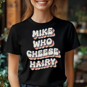 May include: Black t-shirt with a retro-style graphic that says "Mike Who Cheese Hairy".