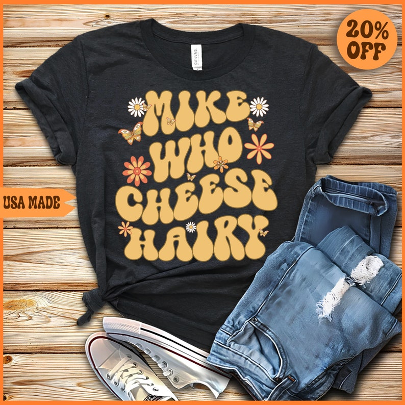 May include: A black t-shirt with a retro-style graphic that says "Make Who Cheese Hairy" in yellow letters with flowers and butterflies around the text.