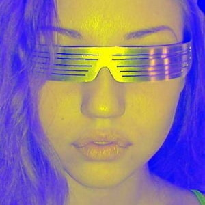 May include: A woman with purple hair wearing silver mirrored sunglasses with a horizontal slat design. The sunglasses are reflecting the light.