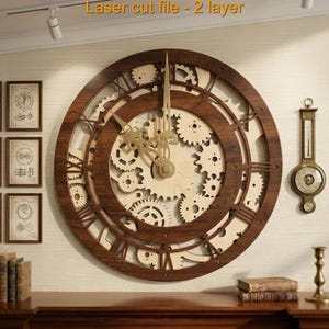 May include: A large circular wall clock featuring a dark brown wooden frame and a light beige wooden interior with intricate laser-cut gear patterns. The clock has ornate gold-colored metal hands and Roman numerals. Text reads: Laser cut file - 2 layer.