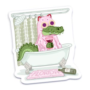 An illustrated sticker of a Florida alligator wearing a pink ghost outfit inspired by a Taylor Swift music video, lounging in a clawfoot bathtub, holding a wine glass, with a "Florida" bathmat and a wine bottle on the floor.