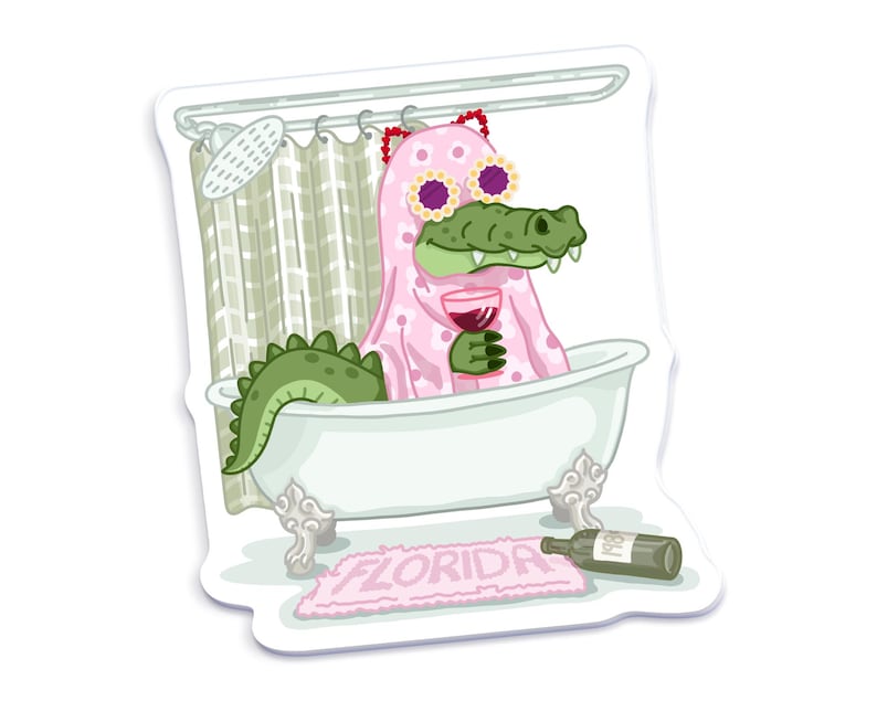 An illustrated sticker of a Florida alligator wearing a pink ghost outfit inspired by a Taylor Swift music video, lounging in a clawfoot bathtub, holding a wine glass, with a "Florida" bathmat and a wine bottle on the floor.