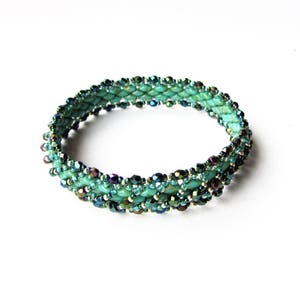 K&ouml;nnte beinhalten: Ein t&uuml;rkisfarbenes und schillerndes Armband mit gewebtem Muster.