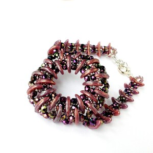 May include: A close-up of a purple and iridescent beaded necklace with a spiral design. The necklace is made with small, faceted beads and has a silver clasp.