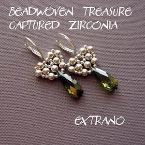 Può includere: Un paio di orecchini in perline argentate con cristalli verdi a forma di goccia che pendono dalla parte inferiore. Gli orecchini hanno la forma di un cuore e hanno il testo "BEADWOVEN TREASURE CAPTURED ZIRCONIA" sopra e "EXTRAN"O sotto.