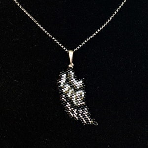 Puede incluir: Un collar de cadena de plata con un colgante de cuentas negras y blancas con forma de ala.