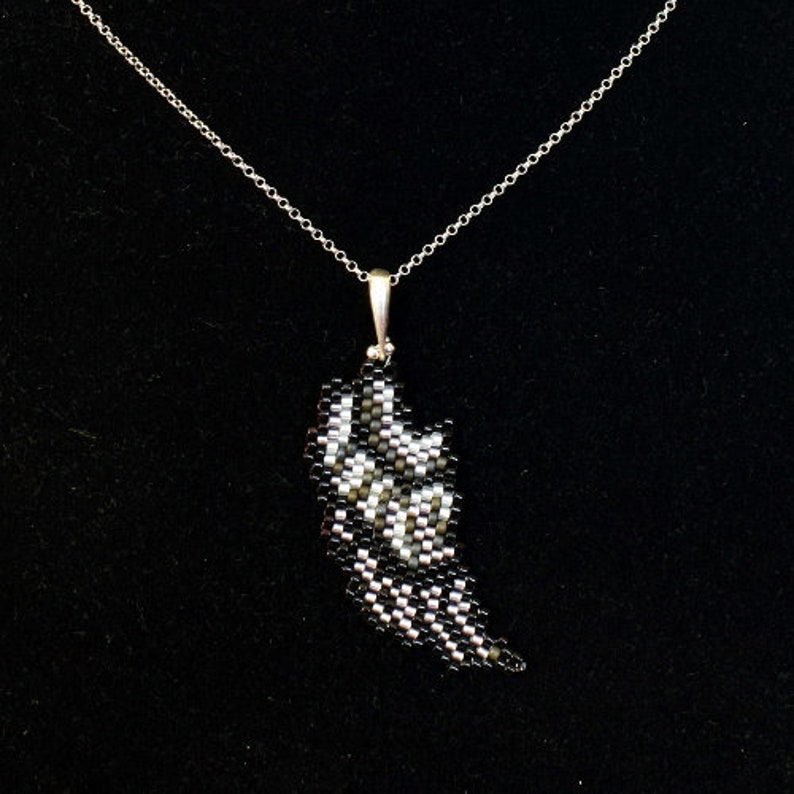 Puede incluir: Un collar de cadena de plata con un colgante de cuentas negras y blancas con forma de ala.