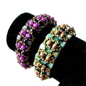 K&ouml;nnte beinhalten: Zwei Perlenarmb&auml;nder, eines mit lila und schwarzen Perlen und das andere mit gr&uuml;nen, kupfernen und schwarzen Perlen.