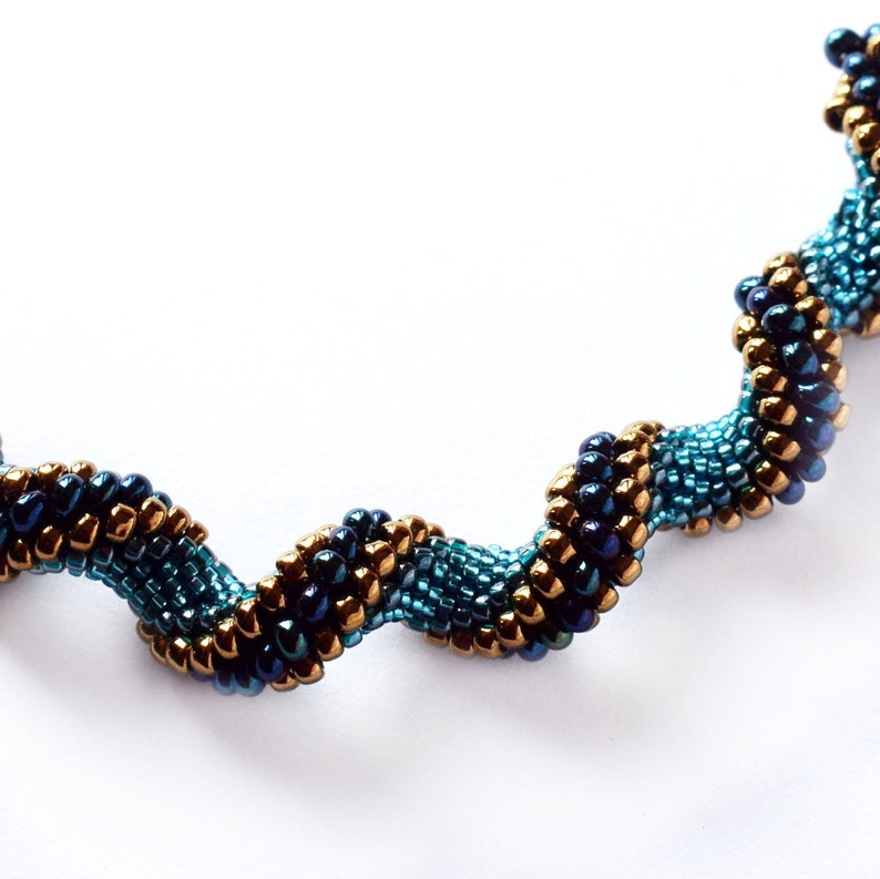 May include: A close-up of a beaded necklace with a spiral design. The beads are a mix of teal, dark blue, and gold.