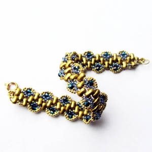 K&ouml;nnte beinhalten: Ein goldfarbenes und blaues Armband mit gewebtem Muster. Das Armband besteht aus kleinen, runden Perlen in Gold- und Blaut&ouml;nen.