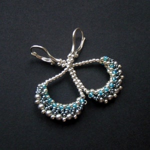May include: Silver earrings with a teardrop shape, made with small blue and silver beads.