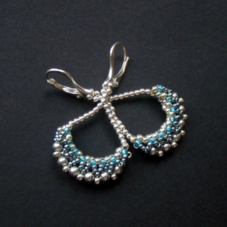 May include: Silver earrings with a teardrop shape, made with small blue and silver beads.
