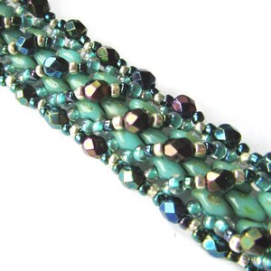 Pu&ograve; includere: Un braccialetto multifilo con perline turchesi, argentate e blu iridescenti. Le perline sono intrecciate insieme in un motivo complesso.