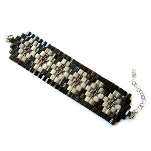 Op de afbeelding: Een zwart-witte kralen armband met een zilveren ketting sluiting. De armband is gemaakt met kleine vierkante kralen in een geruit patroon.