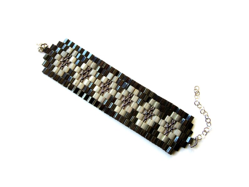 Op de afbeelding: Een zwart-witte kralen armband met een zilveren ketting sluiting. De armband is gemaakt met kleine vierkante kralen in een geruit patroon.