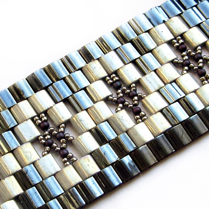 Op de afbeelding: Een zilveren en witte kralen armband met bruine kralen die een geometrisch patroon vormen.