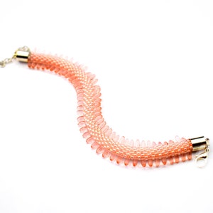 May include: A delicate pink beaded bracelet with a gold clasp. The bracelet is made of small, teardrop-shaped beads that are strung together in a pattern.