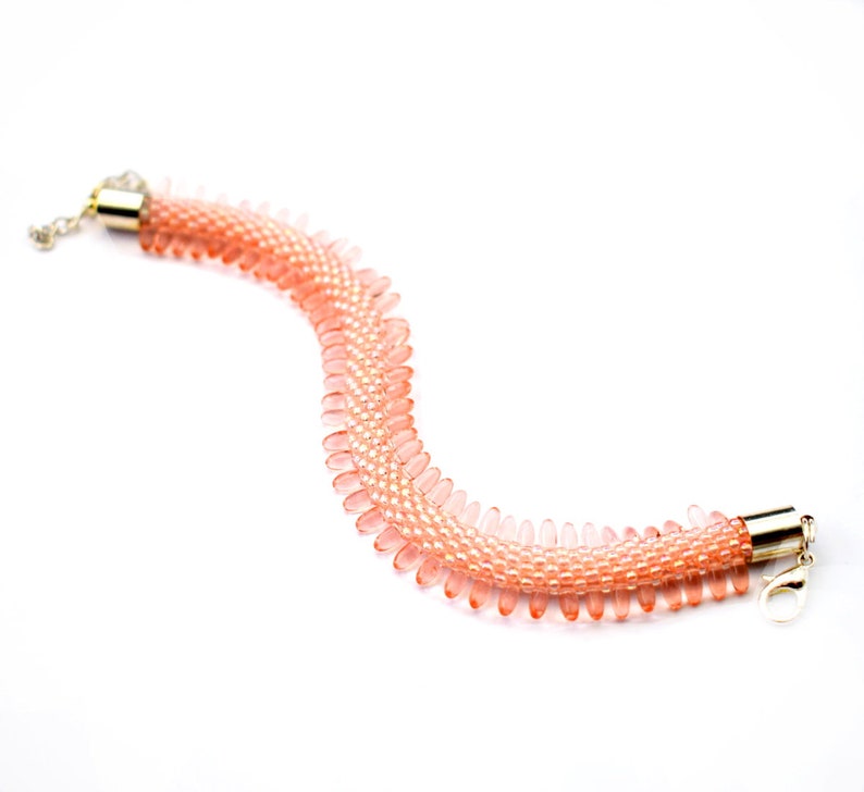 May include: A delicate pink beaded bracelet with a gold clasp. The bracelet is made of small, teardrop-shaped beads that are strung together in a pattern.