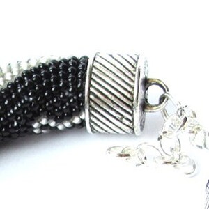 May include: A black, white, and silver beaded necklace with a silver clasp and extender chain.
