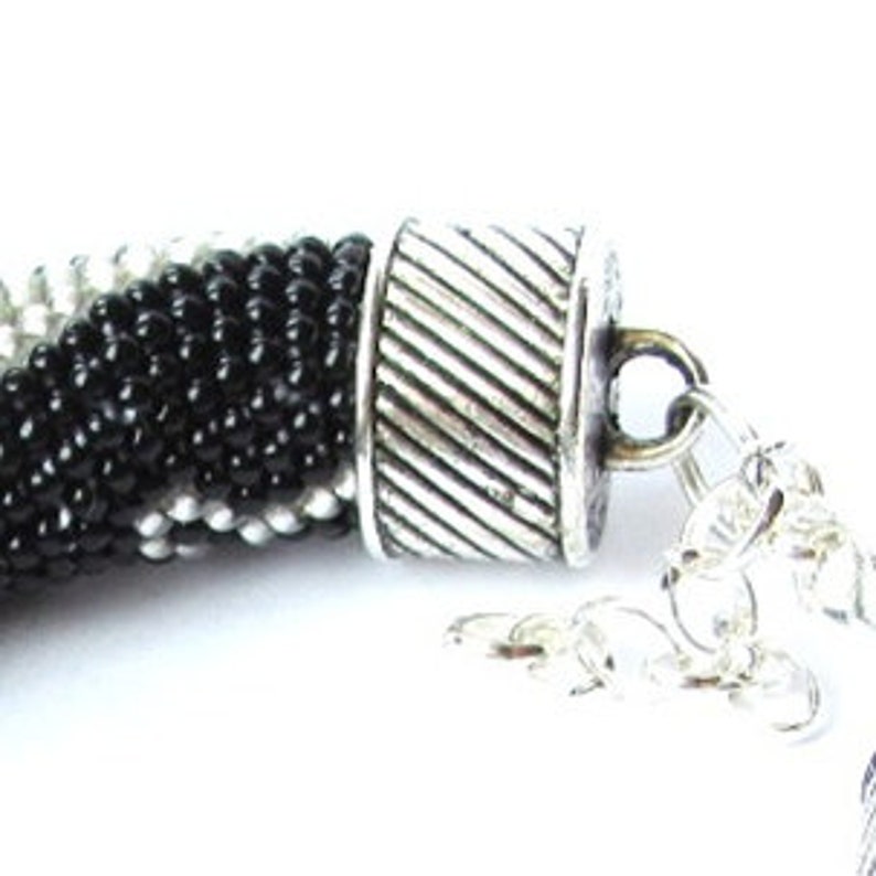 May include: A black, white, and silver beaded necklace with a silver clasp and extender chain.
