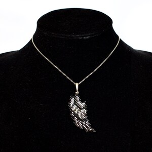 Puede incluir: Un collar de cadena de plata con un colgante de ala de cuentas negras y plateadas.