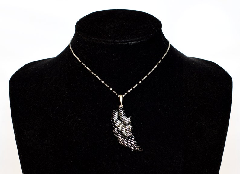 Puede incluir: Un collar de cadena de plata con un colgante de ala de cuentas negras y plateadas.