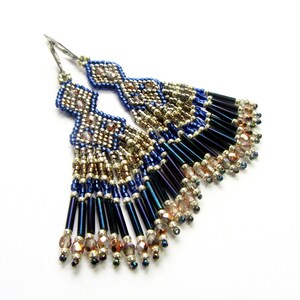 May include: A pair of long, beaded earrings with a geometric design. The earrings are made with blue, silver, and gold beads, and have a fringe of dark blue beads.