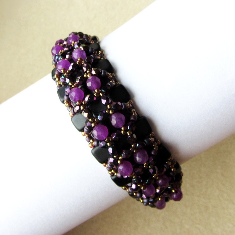 May include: A purple and black beaded bracelet with gold accents. The bracelet is made with small, faceted beads and larger, round beads.