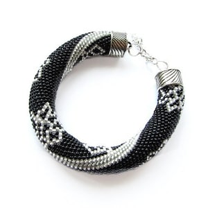 May include: A black and silver beaded bracelet with a silver clasp. The bracelet is made of small beads that are woven together in a pattern.