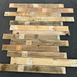 May include: A collection of reclaimed wood planks in various shades of brown, beige, and green. The planks are arranged in a staggered pattern, creating a rustic and natural look.