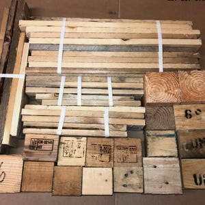 May include: A selection of reclaimed wooden pieces, including planks and blocks, some with stamped markings. The wood is various shades of brown and tan, bundled with white straps, suitable for crafting or rustic decor.