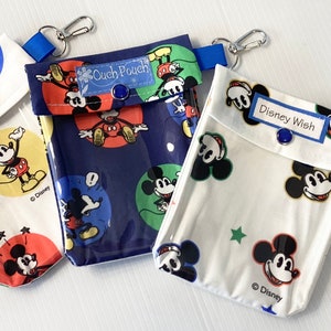 Könnte beinhalten: Drei Beutel mit Mickey Mouse-Designs. Einer ist weiß mit Mickey und Sternen, ein anderer ist marineblau mit Mickey, und der dritte ist weiß mit Mickey und dem Text "Ouch Pouch". Jeder hat einen blauen Riemen und einen silbernen Clip.