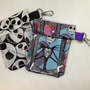 May include: Two small zippered pouches with a clear plastic window. One pouch is black and white with a repeating pattern of Jack Skellington's face. The other pouch is blue, purple, and white with a picture of Jack Skellington. Both pouches have a silver metal clip and a purple strap.
