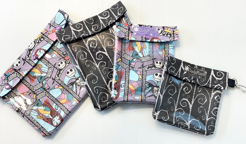 May include: Four clear plastic zipper pouches with different Nightmare Before Christmas fabric designs. The pouches are black with white swirls, black with colorful stained glass designs, and purple with colorful stained glass designs. The pouches have a clear plastic front and a black fabric back. The pouches have a small flap with a snap closure. The pouches have a small tag that says "Clutch Pouch".