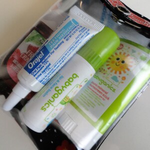 May include: A clear plastic bag containing three different tubes of baby care products. The tubes are labeled "Orajel Oral Pain Reliever", "babyganics Lip & Face Balm", and "babyganics Pure Mineral Sunscreen Stick".