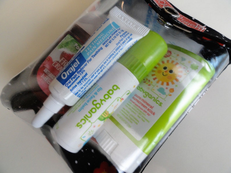 May include: A clear plastic bag containing three different tubes of baby care products. The tubes are labeled "Orajel Oral Pain Reliever", "babyganics Lip & Face Balm", and "babyganics Pure Mineral Sunscreen Stick".