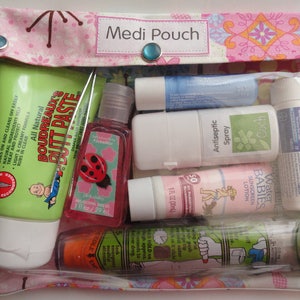 May include: A pink fabric pouch with the words "Medi Pouch" printed on it. The pouch contains a variety of items, including a thermometer, a tube of diaper rash cream, a bottle of hand sanitizer, a tube of sunscreen, a tube of lip balm, a tube of pain relief cream, and a small bottle of antiseptic spray.